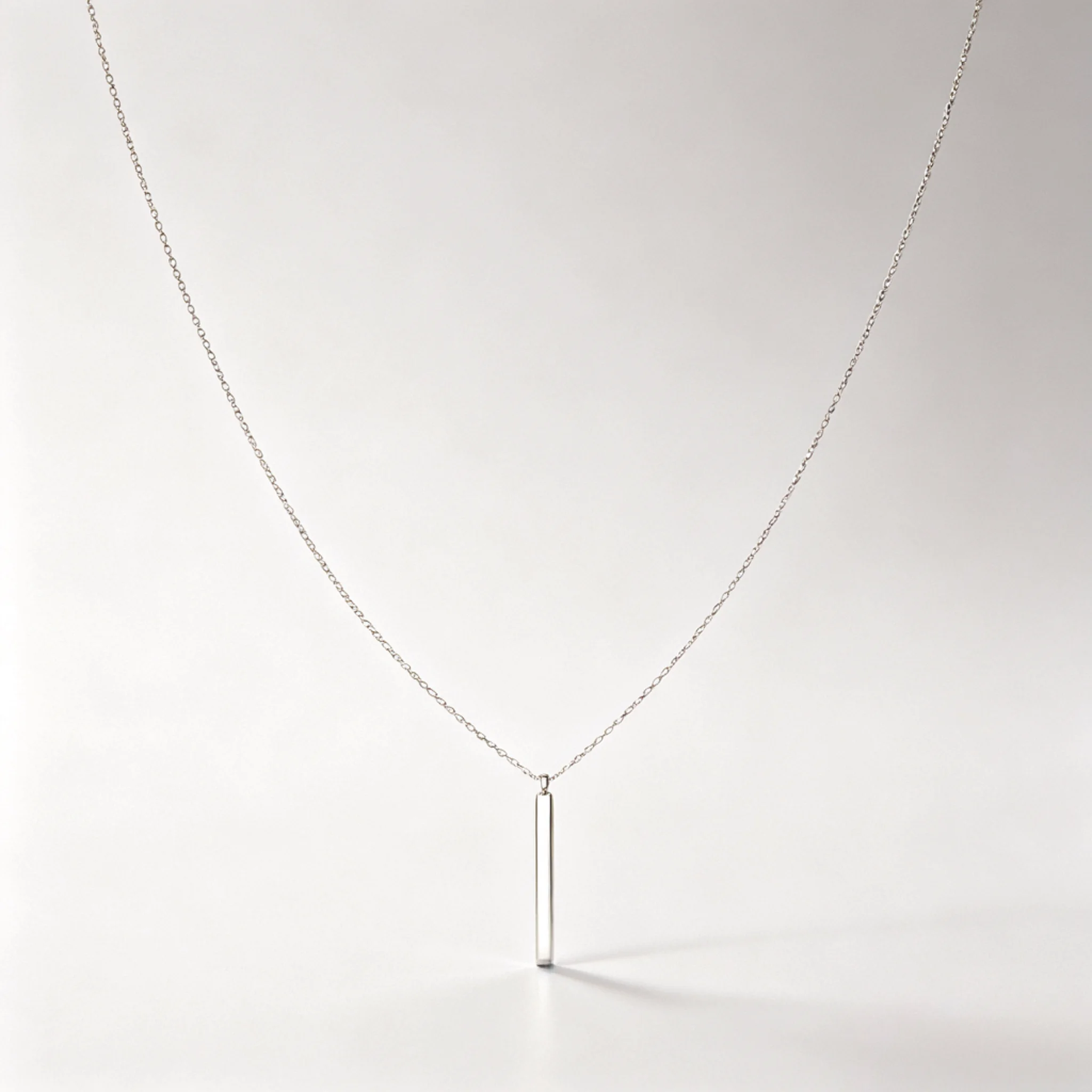 Silver bar necklace laid flat with a narrow plate and matching chain attachments