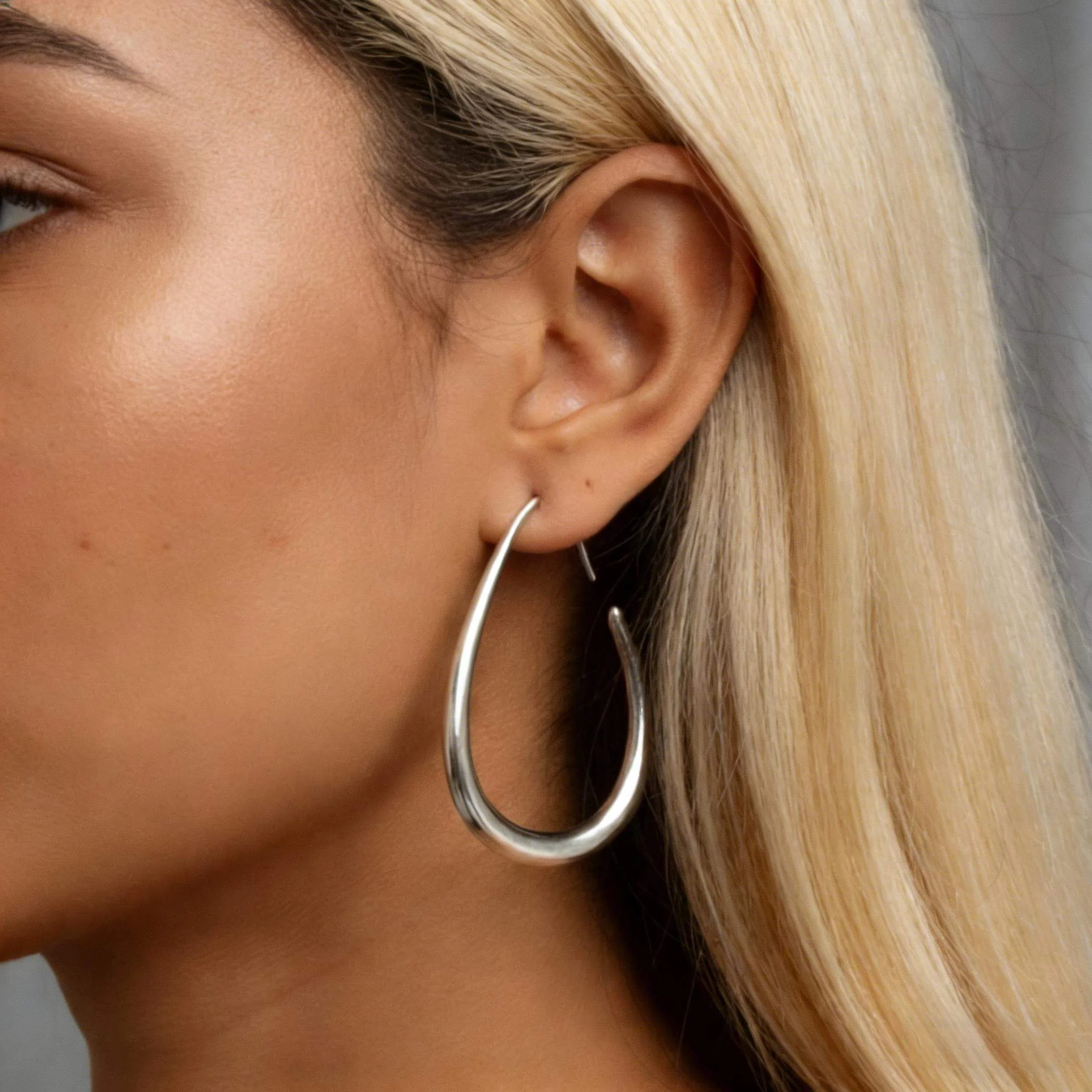 Clean ear close-up of a model wearing silver earrings with crisp edges and reflections.